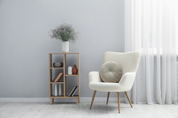 Comfortable armchair and wooden rack with different decor near light gray wall indoors