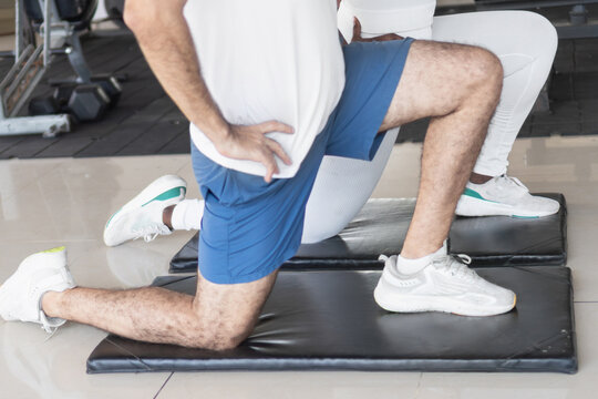 Personal trainer guiding client stretching legs in gym