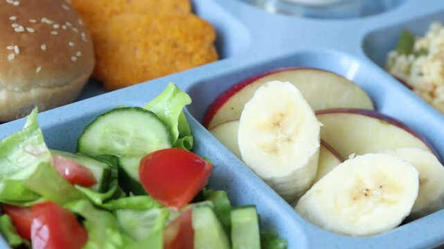 School lunch. Plastic tray with tasty food, milk and fork on wooden table, closeup. Camera moving right