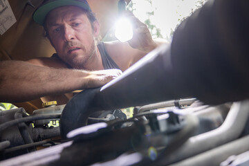 Close-up of a man wearing a cap using a flashlight to inspect a car engine. Detailed view of...