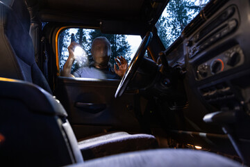 A masked individual shines a flashlight through a car window while peering inside, suggesting a vehicle break-in or attempted theft.
