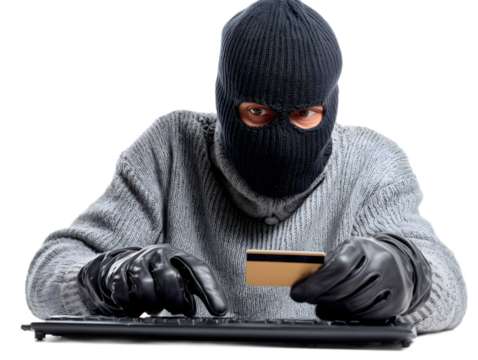 Cybercriminal wearing a balaclava and gloves using a computer keyboard while holding a credit card, representing identity theft, online fraud, cybercrime, and digital financial hacking, isolated on wh
