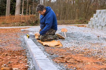 Craftsman prepares ground arranges stones for new patio in residential area surrounded by trees