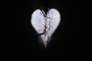Open book illuminated with heart-shaped light and glasses on a black background.