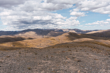 Landscape of the Andean Plateau, mountain range and sparse vegetation with many storm clouds and blue sky