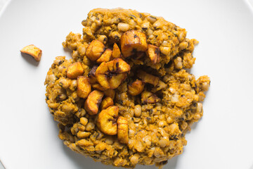Overhead view of nigerian fried beans and fried plantain on a white plate, top view of nigerian stewed beans and plantain on a white background