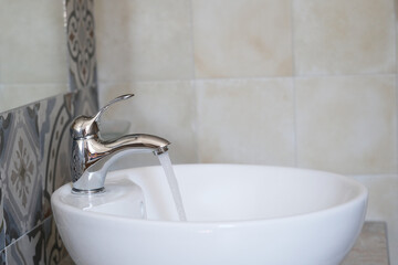 Clear water streams from a polished faucet into a sleek white sink. Waste of resources and Environmental irresponsibility