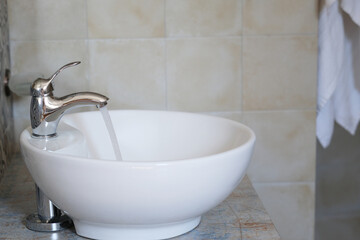 Clear water streams from a polished faucet into a sleek white sink. Waste of resources and Environmental irresponsibility