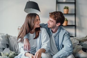 Portrait of young 20s just married couple in love posing photo shooting seated on couch in modern studio apartments, concept of capture happy moment, harmonic relationships, care and sincere feelings
