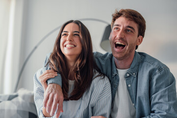 Portrait of young 20s just married couple in love posing photo shooting seated on couch in modern...