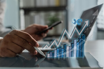 Business growth concept illustrated by rising bar and line charts as a person analyzes financial data using a digital pen and smartphone on a tablet in a modern office environment.