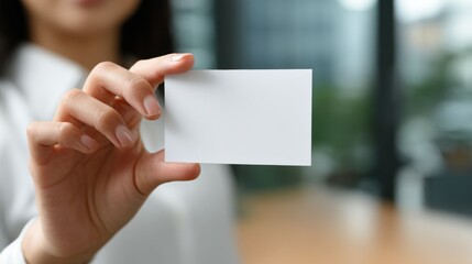 Woman holds blank white business card in hand indoors blurred background.