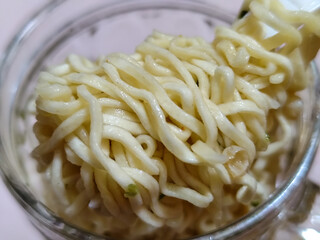 Rolls of springy white instant noodles are lifted with a spoon from the bowl, highlighting their texture and deliciousness, against the blurry background of the bowl.