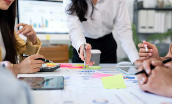 Business professionals collaborating during a meeting. Team members using digital tablets, documents, and charts to analyze data and discuss business strategy.