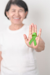 Elderly with light Green Ribbon for concept of May Celiac Awareness month, Lyme disease, September Lymphoma, Mental Health Awareness month and October Liver cancer. Health and world cancer day