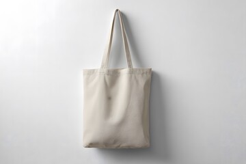 A simple white canvas tote bag hanging against a plain white wall in a studio setting with soft lighting