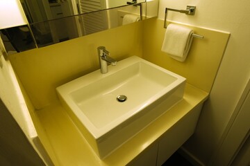 Top-down view of a modern rectangular sink with chrome faucet, mounted towel, and large mirror in a clean bathroom.
