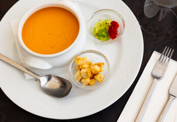 Cold soup gazpacho in bowl served with vegetables, baked breads and olives on table in restaurant