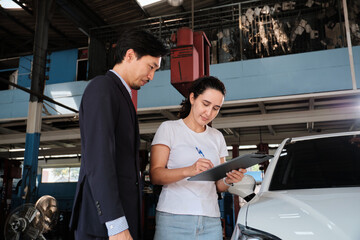 Warranty service business work, Latino female client cheerful inspections sign contract document from Asian male insurance agent, accept claims car fix from accident and maintain at automotive garage.