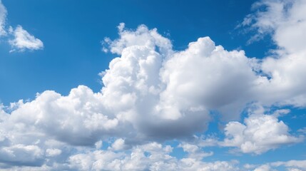 Fototapeta premium Fluffy white clouds drift lazily in the bright blue sky, creating a tranquil scene on a sunny afternoon. The ambiance suggests a peaceful and refreshing atmosphere.