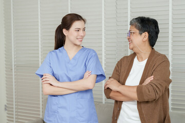 Fototapeta premium Elderly Asian woman and female physiotherapist stand side by side with arms crossed smiling showing confidence satisfaction and trust after therapy session