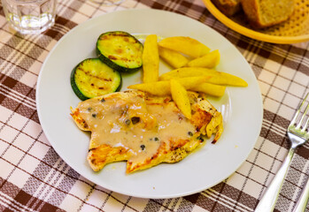 Chicken breast with white sauce with pepper, served with side dish of French fries and fried piece of zucchini. Hearty dish of poultry meat and vegetables