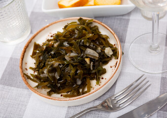 Portion of just cooked salad made of sea cabbage, laminaria, and onion, served on plate.
