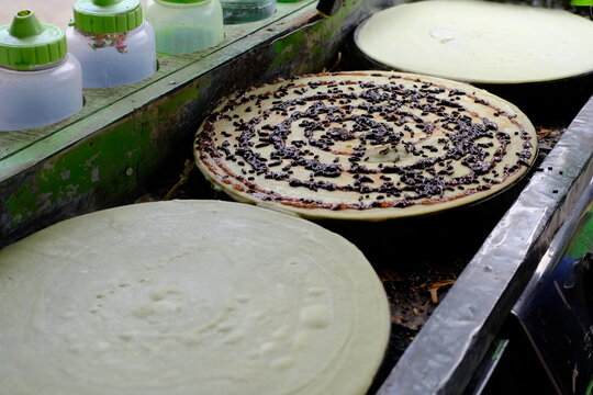 Fresh Indonesian leker crepes being prepared on a hot griddle, with chocolate sprinkles added as a sweet filling.
