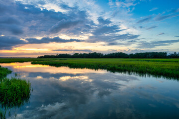 Sunset over a tranquil river with lush greenery and vibrant clouds in the sky
