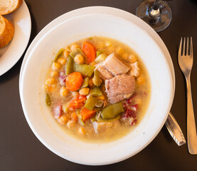 Plate with portion of hot chickpea and meat soup. First course is served with pieces of baguette..