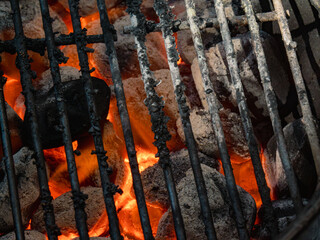 glowing red charcoal briquettes beneath the well-used metal grates of a barbecue grill