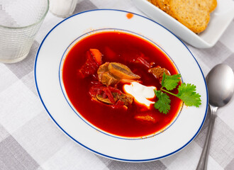 Traditional thick beetroot soup with beef served with sour cream and fresh greens for lunch..