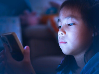 Asian girl using smartphone at night with glowing screen, concept of screen addiction and harmful blue light in children