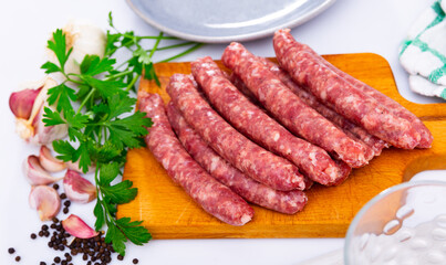 Pile of popular Spanish raw sausages longaniza with fresh greens, garlic and spices prepared for cooking on wooden cutting board with knife. Traditional meat products
