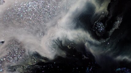 Macro shot of black and grey glitter ink spreading through a milky liquid, pushed by injected air in a dynamic motion.