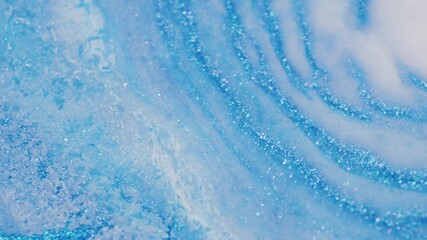 Macro shot of blue glitter ink being pushed aside by a milky liquid introduced from the top right, creating soft fluid movement.