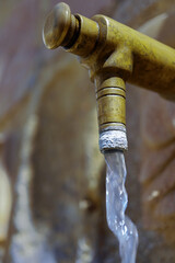 Close-up of an old brass faucet pouring fresh water, providing hydration in a public space