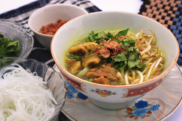 Savory Asian soto food with tender chicken, fresh herbs, crispy fried shallots, and rich aromatic broth, served with rice noodles and vibrant garnishes for a flavorful traditional indonesia meal