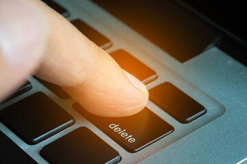 Finger of the computer user, he presses the delete button on the computer keyboard.