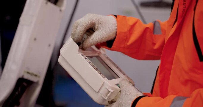 Close up of handheld robot controller with visible buttons and screen operated by gloved engineer during industrial robotics training session in automation lab for interface practice and diagnostics