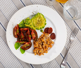 Healthy hearty breakfast of buckwheat porridge with ripe avocado, tomato dressed with fragrant basil pesto sauce and chorizo slices