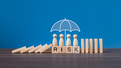 A business team at the workplace is protected under an umbrella while falling dominoes are stopped, illustrating risk management, insurance protection, and safety strategy in organizations