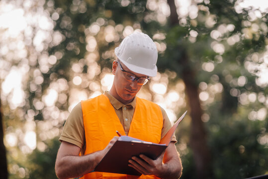 Forestry engineer taking notes on clipboard while inspecting trees in park