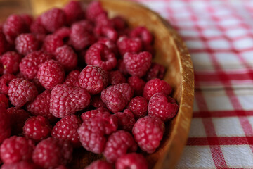 A wooden bowl with ripe raspberries lies on a rustic tablecloth.