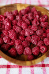 A wooden bowl with ripe raspberries lies on a rustic tablecloth.