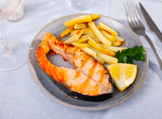 Delicious spanish dish, grilled salmon with fries potatoes served with lemon and parsley in restaurant