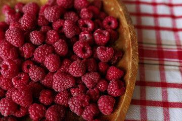 A wooden bowl with ripe raspberries lies on a rustic tablecloth.