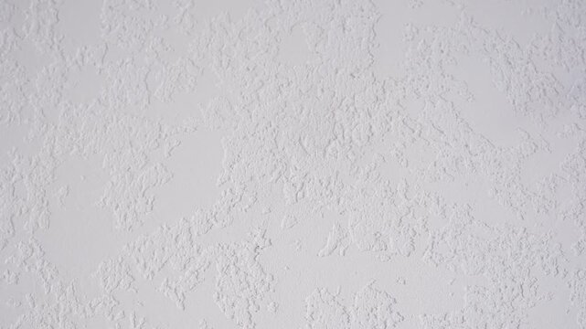 This bright white wall surface features a rough, stippled texture. The irregular pattern creates an abstract background ideal for various designs.