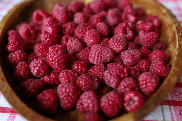 A wooden bowl with ripe raspberries lies on a rustic tablecloth.