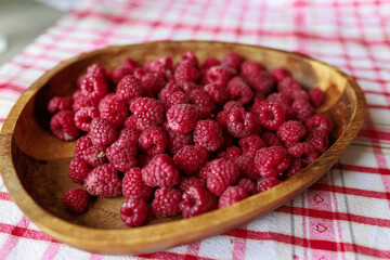 A wooden bowl with ripe raspberries lies on a rustic tablecloth.